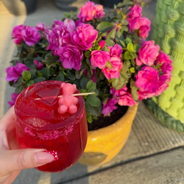 A ruby-red cocktail with a gummy-bear garnish out on the patio